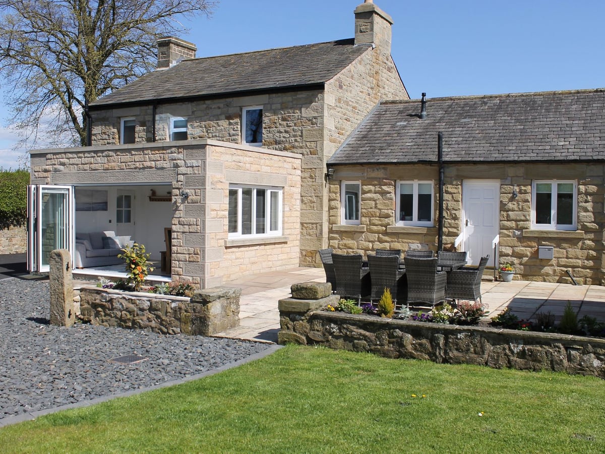 Vine Cottage rear stone walls, glazed doors and dining patio beside a small lawn