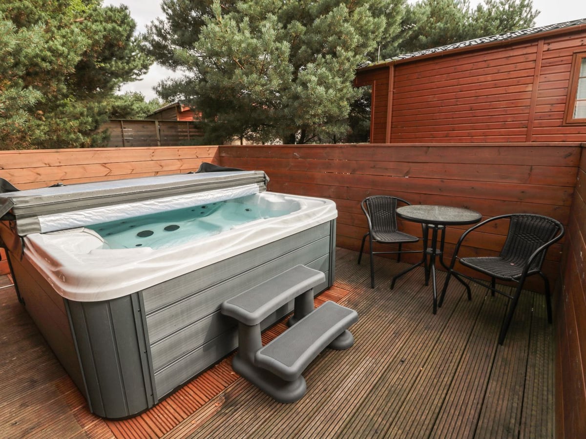 Hot tub and small dining table on the timber deck at Welcome Hjem Log Cabin.