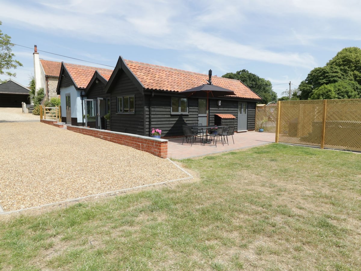 Whitehands Farm Barn with black timber walls, a red-tiled roof, patio seating and lawn