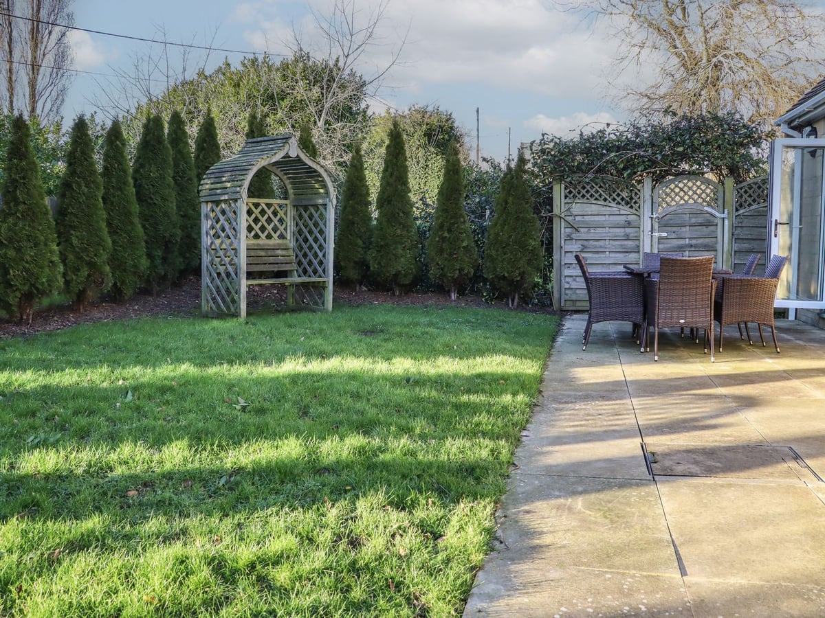 Willow Cottage garden with lawn, a wooden arbour and a dining table beside the patio doors