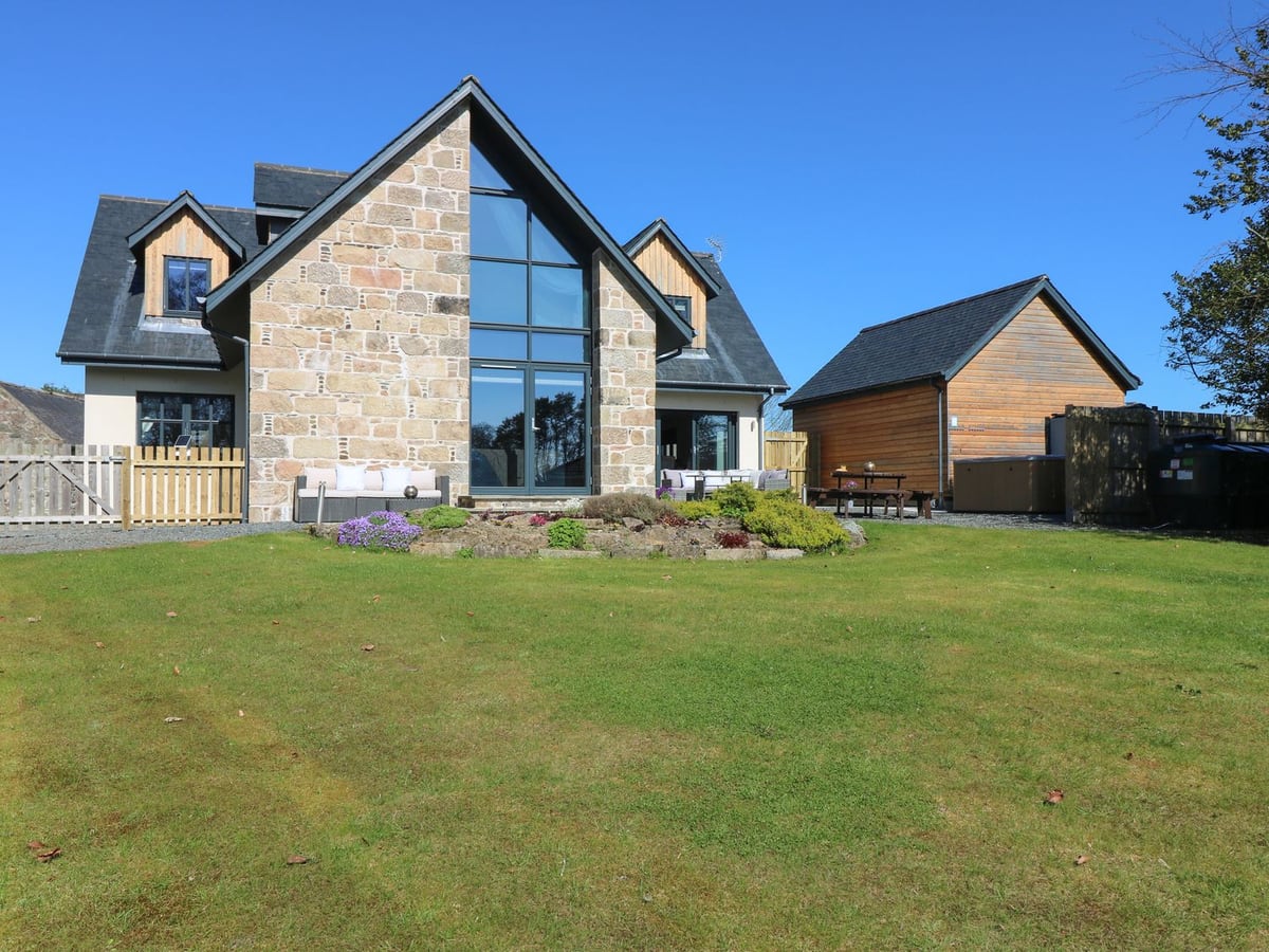 Woodend Croft with a broad lawn, tall glazed gable and outdoor seating beside the house