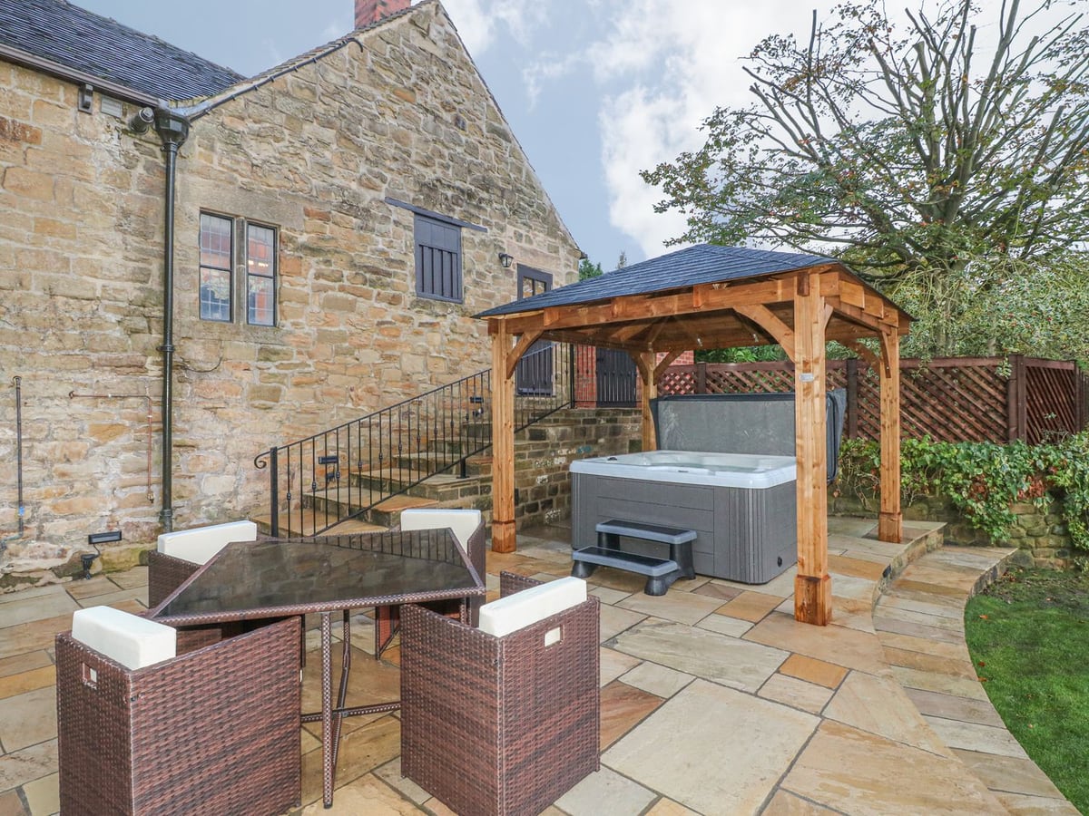 Woodland Lodge patio with a covered hot tub, stone walls, dining table and a strip of lawn
