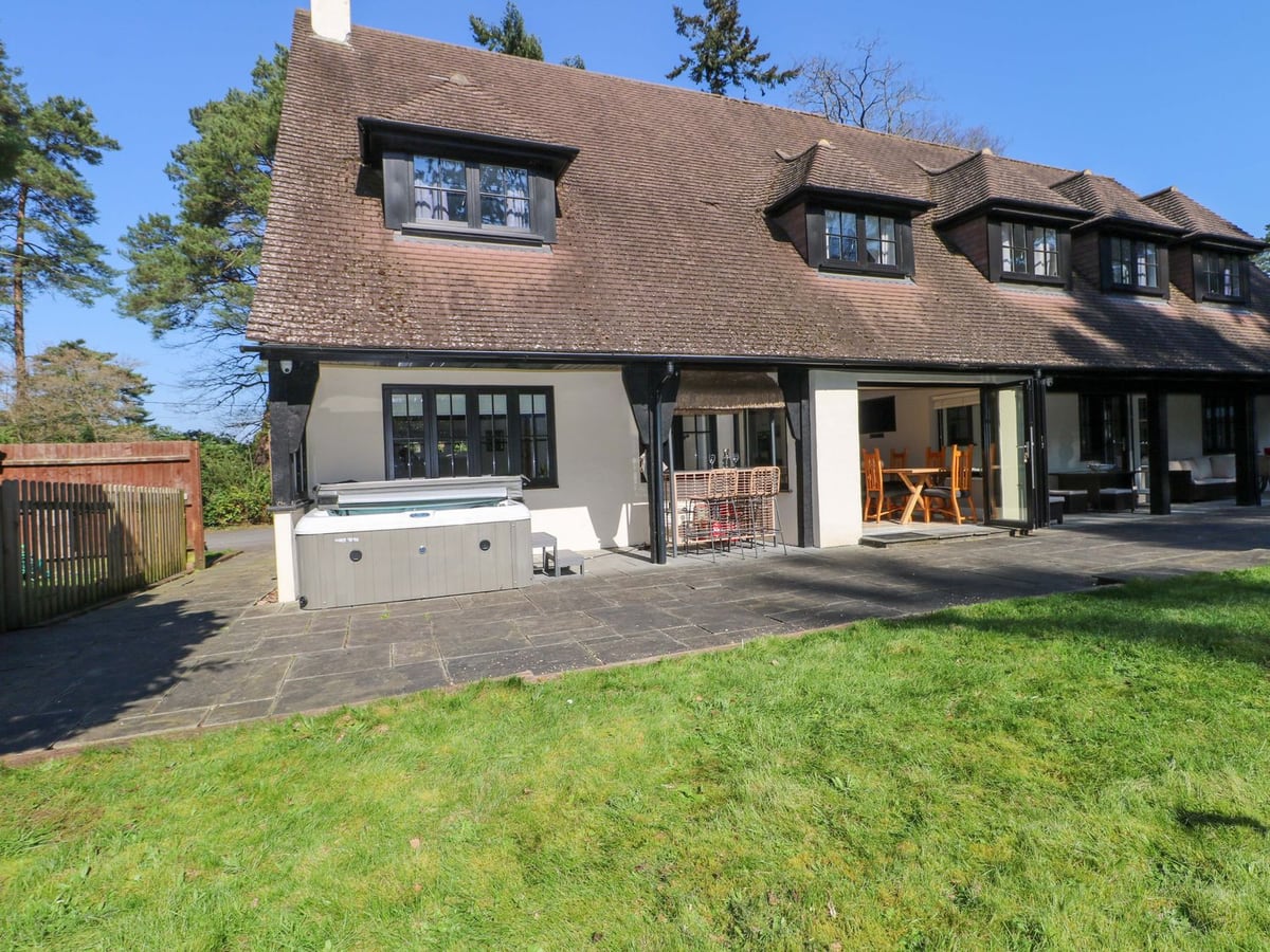 Lawn, paved terrace and hot tub beside the rear doors and covered seating at Woodlands House