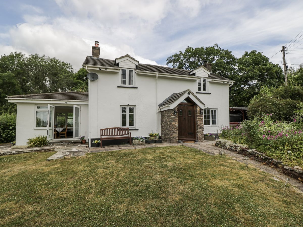 Woods Cottage white house with a front lawn, bench, stone porch and flower border