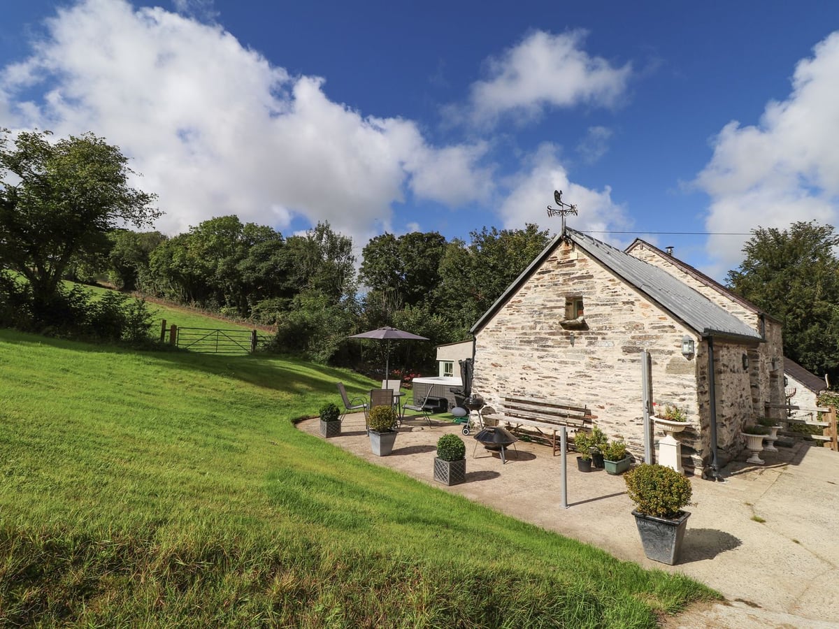 Y Felin at Coed Cadw with a sloping lawn and furnished patio beside the stone cottage