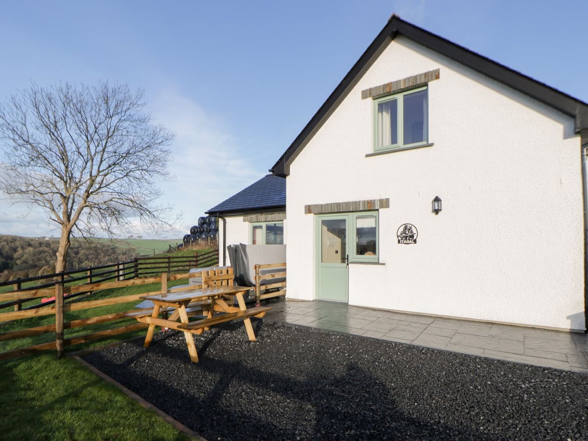 Y Stabal's white gable end with a paved patio, picnic bench on gravel and a post-and-rail fenced lawn