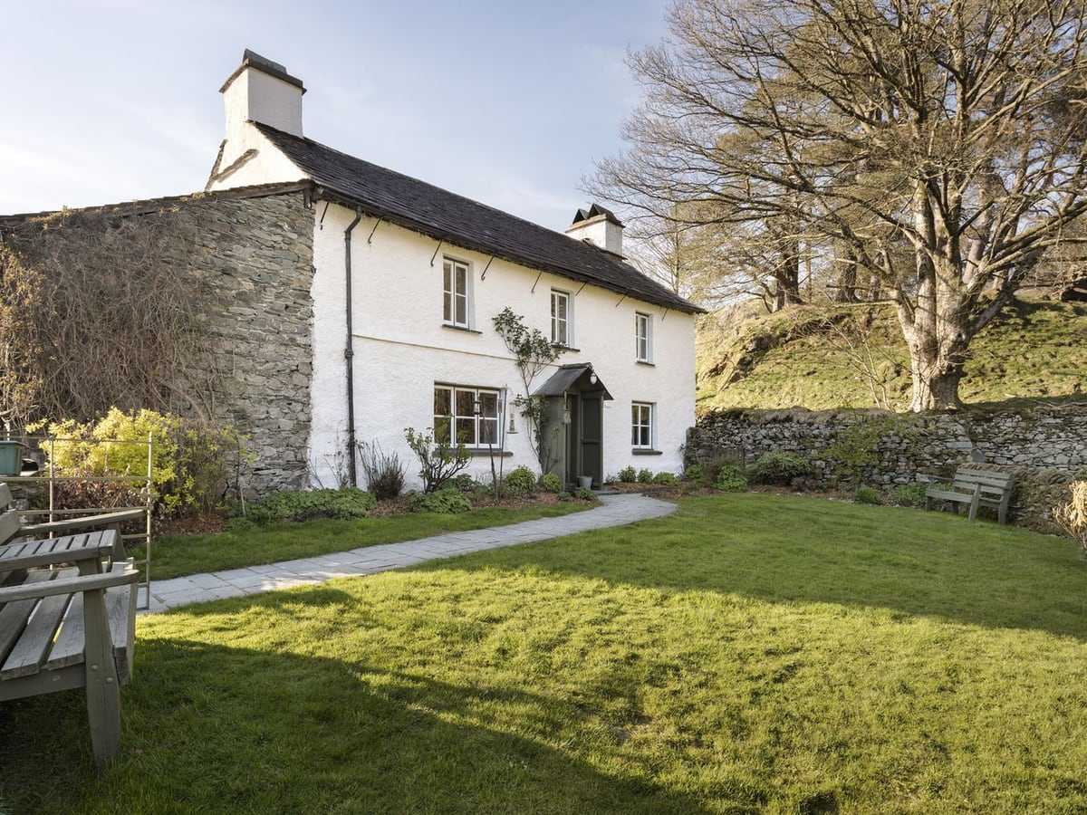 Yew Tree Farm with white walls, a slate roof and a lawn bordered by stone walls and trees