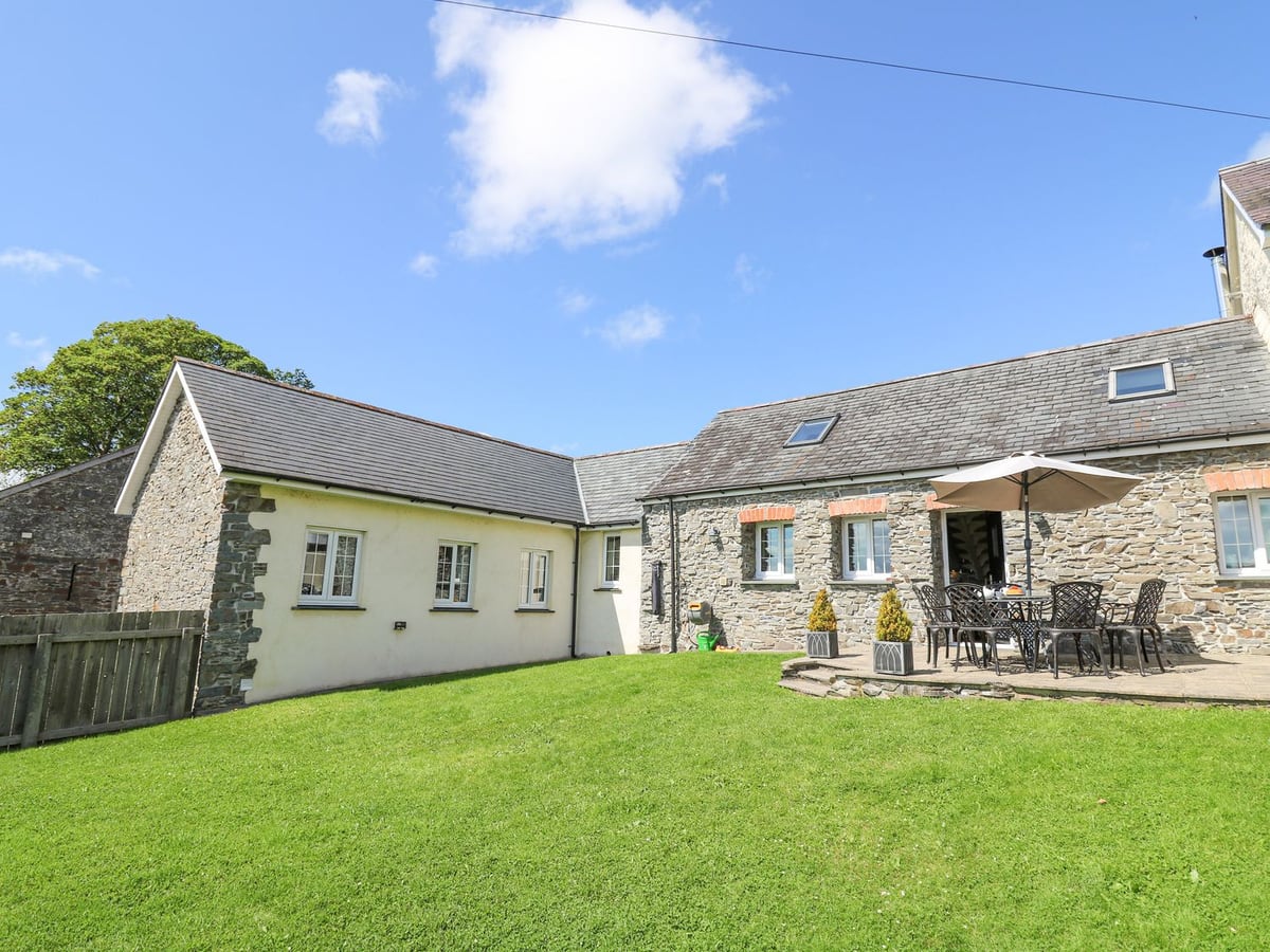 Yr Hen Beudy stone and rendered cottage with a lawn, patio dining set, parasol and wooden fence