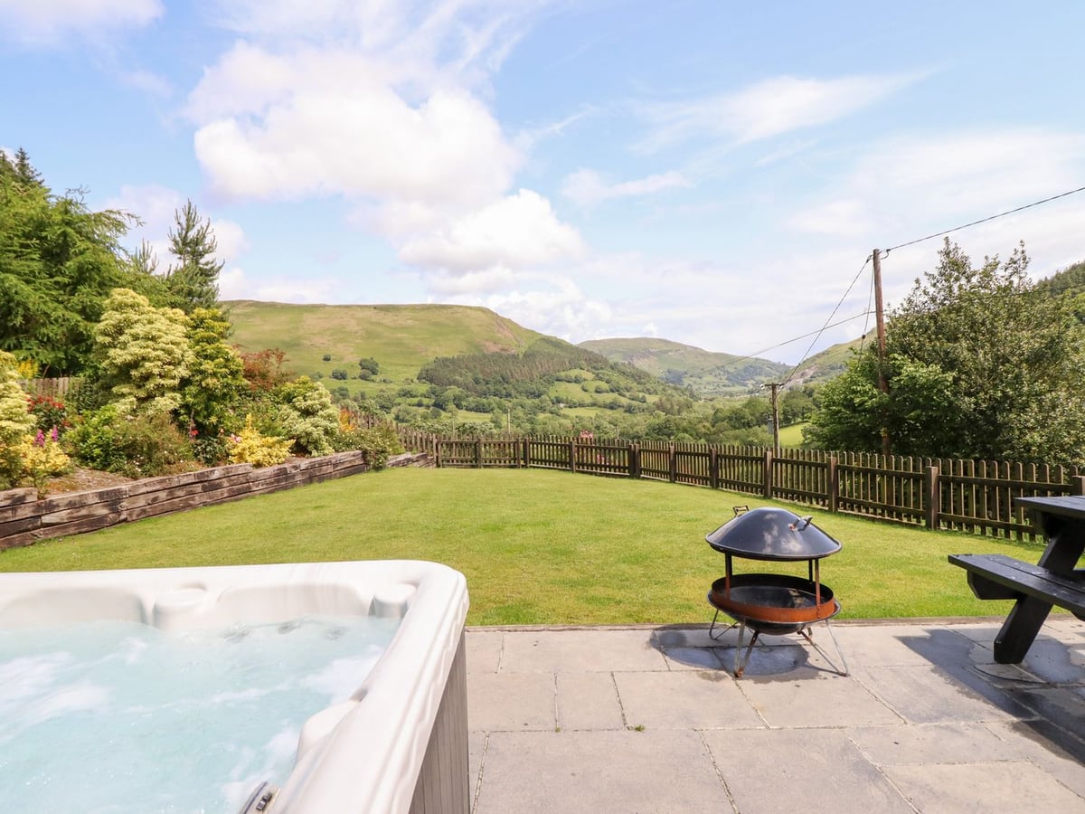 Ysgubor Pwlliago hot tub beside fenced lawn, picnic table, and valley hills